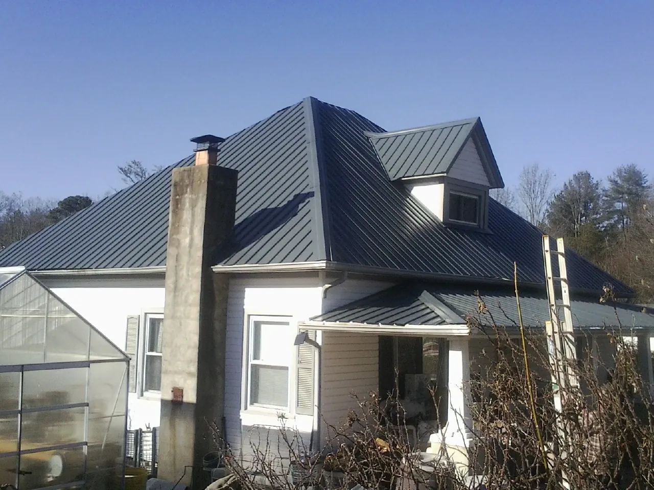 Dark blue standing seam metal roof on a white farmhouse with dormer — Slate & Tile Roof Repair by Roofing Brothers in New Laguna