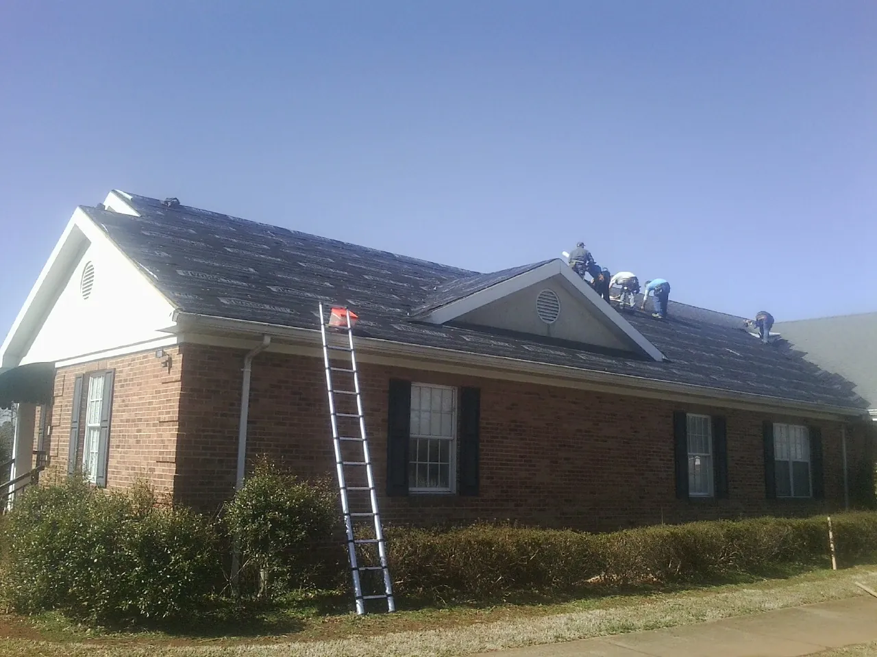 Crew tearing shingles off a brick ranch roof with a ladder set — Metal Roof Repair work by our crew in New Laguna