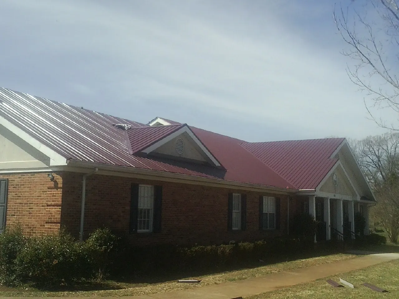 Red metal roof with gabled entries on a long brick building, from a Hail Damage Roof Repair job in New Laguna