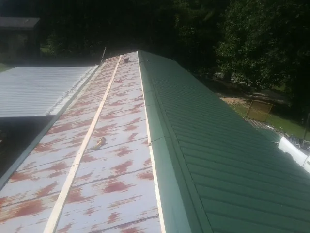Old rusted panels beside newly installed green metal roofing — Wind Damage Roof Repair by Roofing Brothers in New Laguna