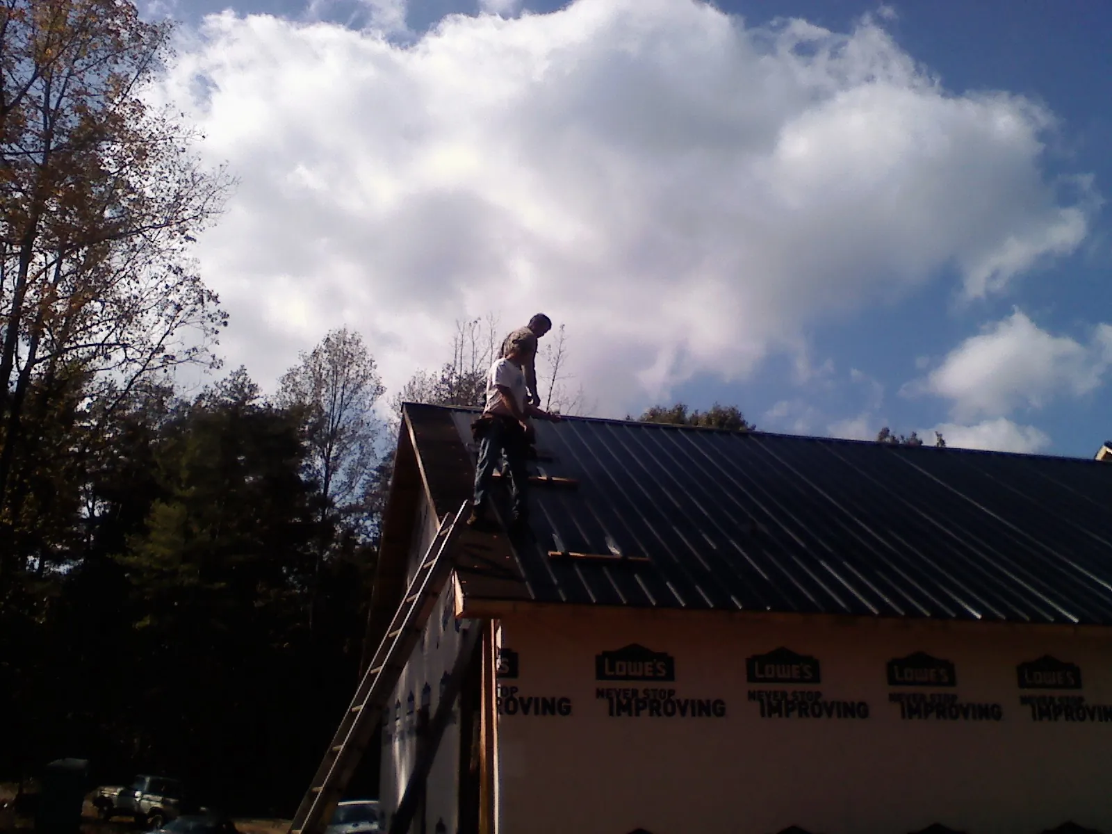 Roofer fastening dark metal panels high against a cloudy sky, from a Roof Inspection job in New Laguna