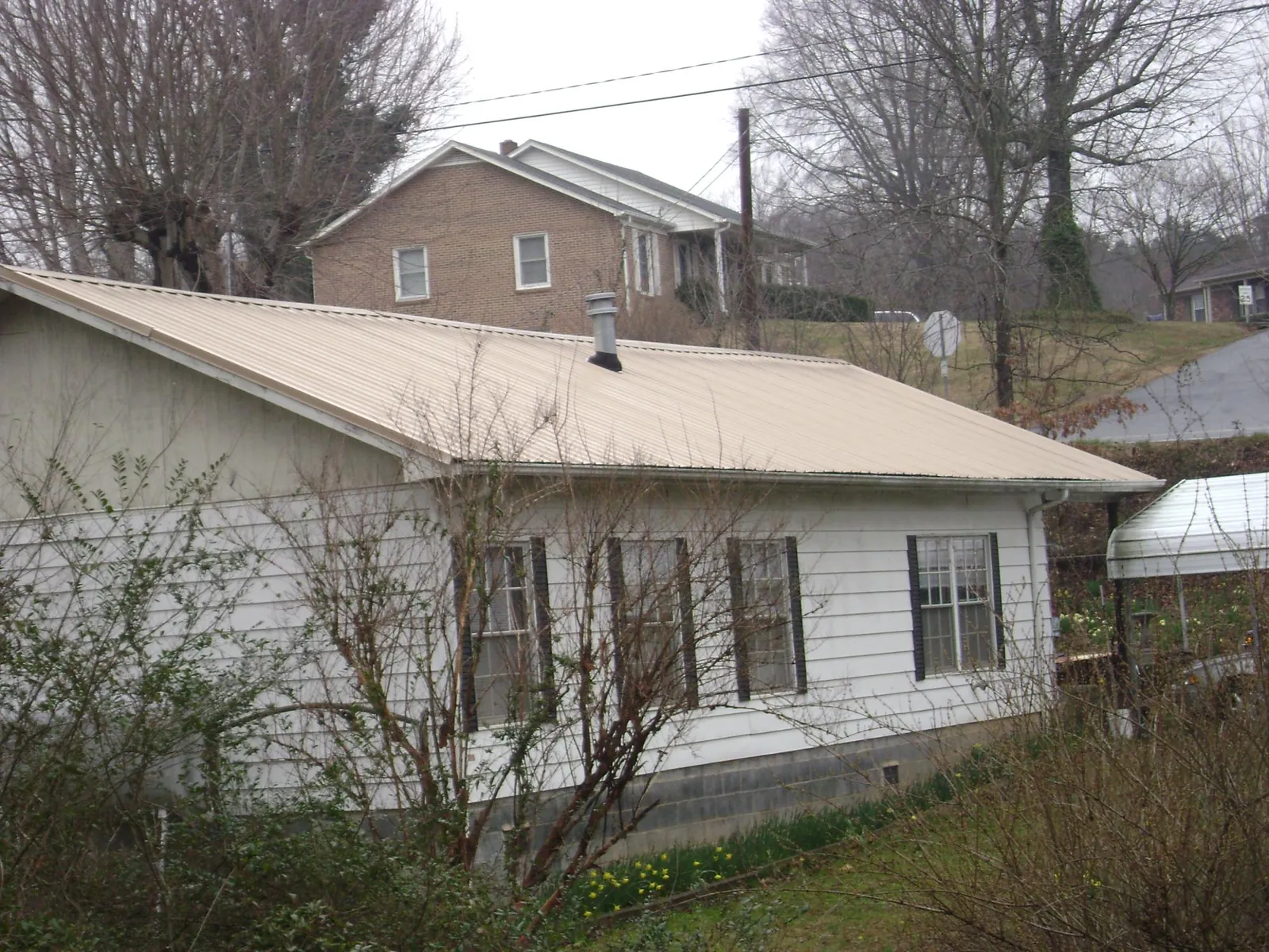 Tan metal roof on a white sided house set into a hillside — Commercial Roofing by Roofing Brothers in New Laguna